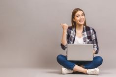 a woman sitting on the floor with her laptop in front of her and pointing up