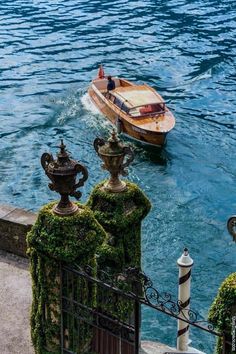 a small boat in the water next to a fence with moss growing on it's sides