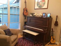 a living room with a piano, couch and guitar on the wall next to it