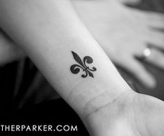 a small black fleur de lis tattoo on the wrist