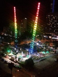 an amusement park at night with ferris wheel lit up in bright colors and buildings behind it