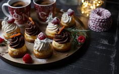 small cupcakes with whipped cream and raspberries on a plate next to two cups of coffee