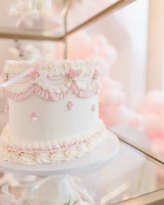 there is a white cake with pink flowers on the top and bottom, sitting on a glass stand