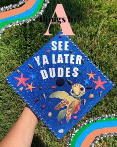 a hand holding a blue graduation cap that says see ya later dudes on it