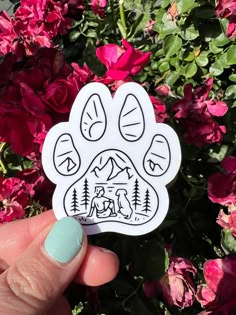 a hand holding up a sticker with a dog's paw and mountains in the background