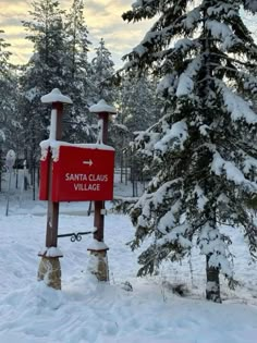 a red sign sitting in the middle of a snow covered field next to a pine tree