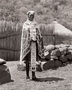 an old photo of a man in native clothing standing next to some rocks and grass