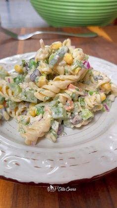 pasta salad with corn and green onions on a white plate sitting on a wooden table