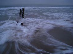 an ocean with waves coming in to shore and wooden posts sticking out of the water