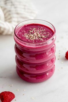 raspberry smoothie in a glass jar with strawberries around it on a white surface