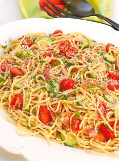 a plate of pasta with tomatoes and zucchini on it next to a fork