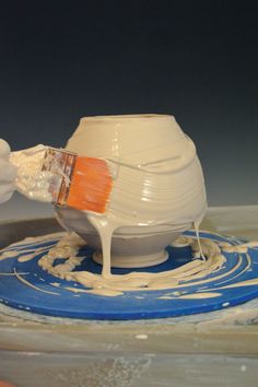 a person is painting a white vase with orange and blue paint on the top,