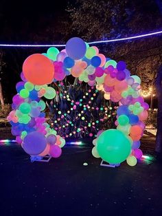 a bunch of balloons that are on the ground in front of a tree at night