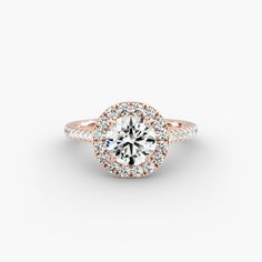 a rose gold engagement ring with round diamonds on the band and an halo setting in the center