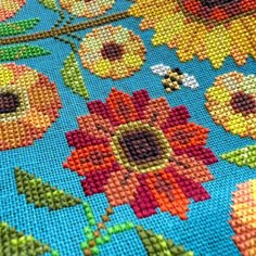 a cross stitch pattern with flowers and bees on blue groundclothe, close up