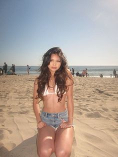 a woman sitting on top of a sandy beach next to the ocean with people in the background