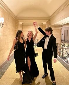 three people dressed in formal wear are dancing on the floor with their arms up and one person is wearing a tuxedo