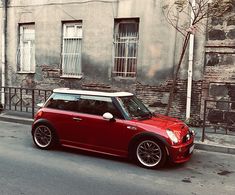 a small red car parked on the side of the road in front of a building