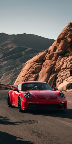 a red sports car driving down a road next to some rocks and a mountain in the background