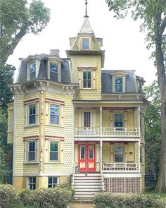 a large yellow house with red door and stairs in front of it, surrounded by trees