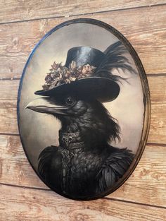 a black bird with a hat and flowers on it's head hanging from a wooden wall