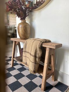 a wooden bench sitting in front of a mirror on top of a checkered rug