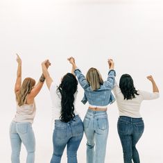 four women are standing together and raising their arms in the air with one woman's back to the camera