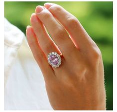 a woman's hand holding a ring with an oval shaped pink sapphire surrounded by smaller round diamonds