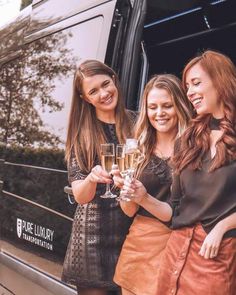 three women standing next to each other holding wine glasses in front of a tour bus