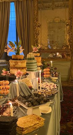 an assortment of desserts and pastries on a table in a room with curtains