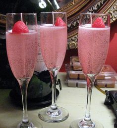 three wine glasses filled with pink liquid and topped with strawberries, sitting on a counter