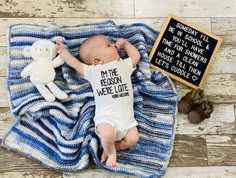 a baby laying on top of a blanket next to a teddy bear and chalkboard