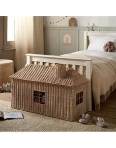 a wicker doll house sitting on the floor next to a bed