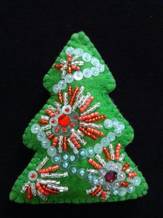 a small christmas tree made out of buttons and beads on a black background with an orange bead decoration