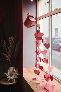 pink paper hearts hanging from a window sill next to a vase with flowers in it