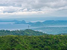 a view of the ocean and mountains from atop a hill with trees on each side