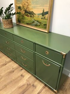 a green dresser with a painting on the wall above it and a basket next to it