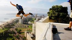 two people are standing on the edge of a building and one person is jumping in the air