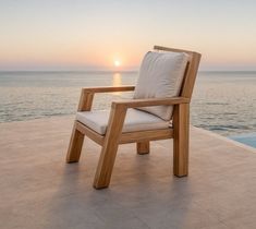 a wooden chair sitting on top of a cement floor next to the ocean at sunset