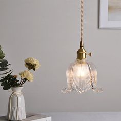 a white vase with flowers in it next to a light fixture on a table top