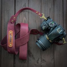 a camera with a strap attached to it sitting on a wooden floor next to a leather camera case