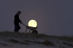 a man pushing a wheelbarrow with the moon in the background