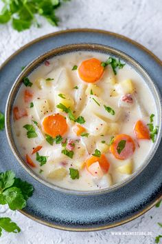 a bowl of soup with carrots, potatoes and parsley in it on a blue plate