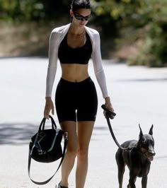 a woman walking her dog on a leash down the street while wearing black sports bra top and shorts