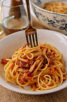 a fork is stuck into spaghetti in a white bowl with bacon and tomato sauce on it