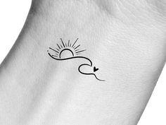 the back of a white arm with a small sun and arrow tattoo design on it