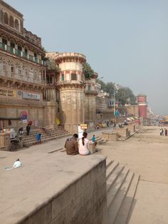 two people sitting on the edge of a concrete wall next to some stairs and buildings