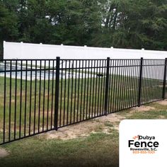 a black fence is in front of a white building and some green grass with trees behind it