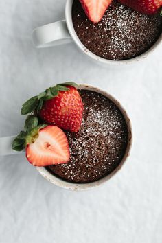 two mugs filled with brownie and strawberries on top of a white table