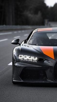 an orange and black sports car driving down the road